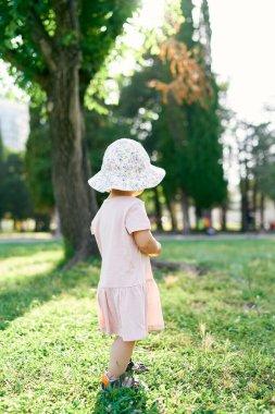 Parktaki yeşil çimlerin üzerinde duran şapkalı küçük kız. Arka plan