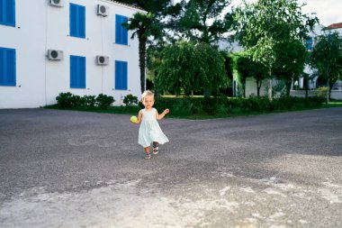 Elinde bir topla evin asfalt bahçesinde yürüyen küçük bir kız.