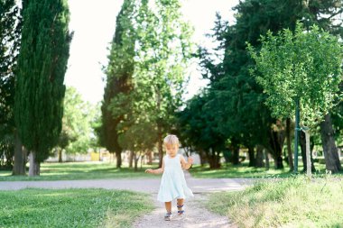 Yeşil bir parkta, yeşil elbiseli küçük bir kız yürüyor.