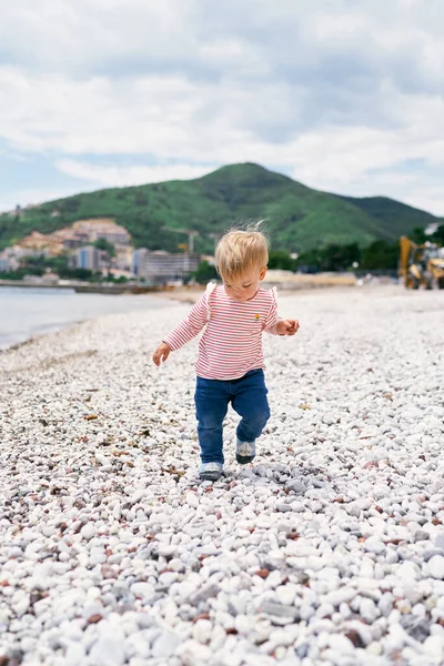 Anak kecil berjalan di sepanjang pantai kerikil melihat kakinya — Stok Foto