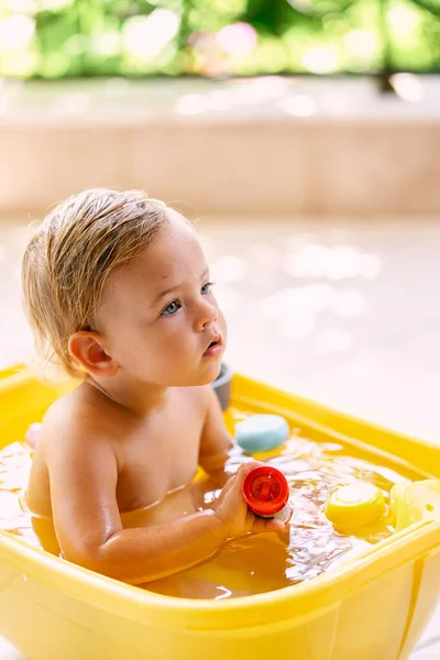 Bambino siede in una ciotola d'acqua e tiene in mano un giocattolo — Foto Stock