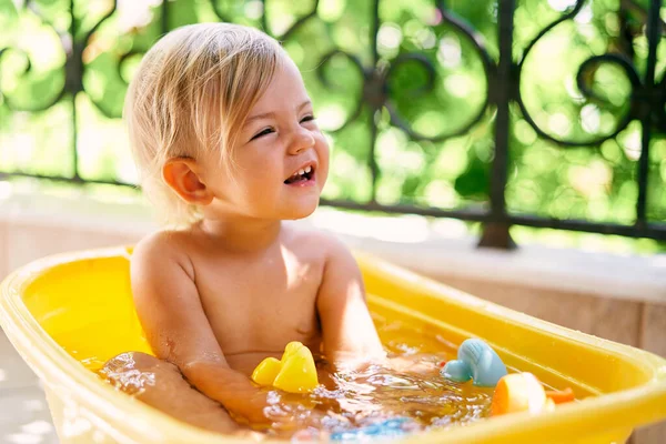 Ragazzo sorridente seduto in una ciotola con acqua e giocattoli sul balcone — Foto Stock