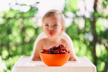 Kirli bir çocuğun önünde, balkondaki masada meyveli kase.