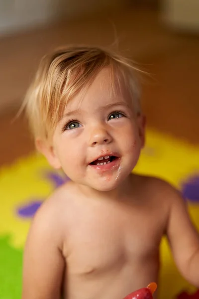 Laughing little kid with dirty face and ice cream in hand sits on the floor — ストック写真