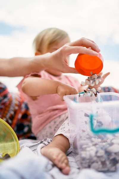 Woman hand pours small stones into a plastic bucket next to the child. Close-up — 스톡 사진