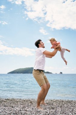 Babam çakıl taşı plajında duran küçük bir kızın etrafında dönüyor.