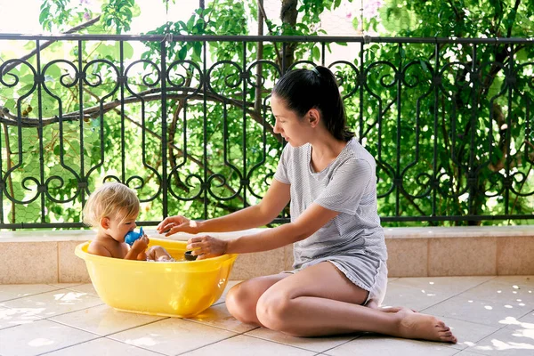 Mom sits on the floor next to a little girl in a basin on the balcony — 스톡 사진