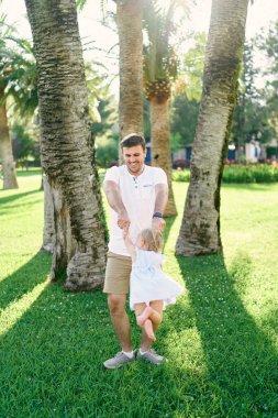 Babam yeşil çimenlikteki palmiye ağaçlarının altında küçük bir kızın etrafında dönüyor.