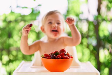 Masadaki meyvelerin önünde oturan gülümseyen çocuk.