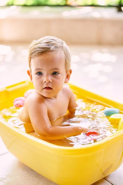 Il bambino si siede in una ciotola d'acqua e distoglie lo sguardo — Foto Stock