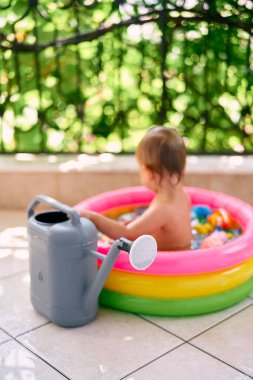 Büyük bahçe sulama kutusu şişme bir havuzda oturan bir çocuğun arka planında duruyor.