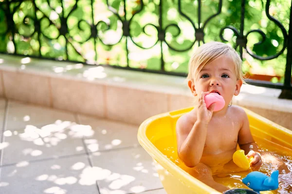 Piccolo bambino si siede in una ciotola d'acqua e rode un'anatra di gomma — Foto Stock