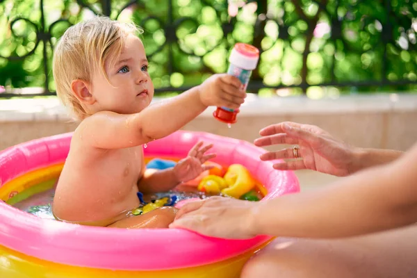 Carino bambino bagnato si siede in una piccola piscina gonfiabile con giocattoli — Foto Stock