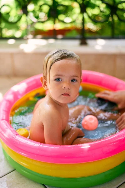 Cute baby sits in inflatable mini pool, turning back — Stock Photo, Image