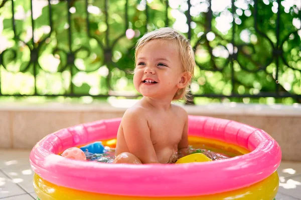 Pequeno bebê sorridente senta-se em uma pequena piscina inflável — Fotografia de Stock