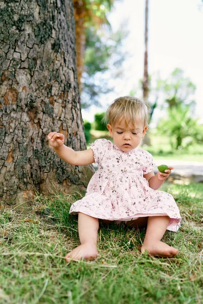 La bambina si siede vicino a un platano — Foto Stock