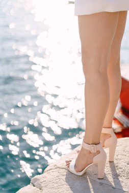 Denizin arka planında topuklu ayakkabı giyen ince bacaklı bir kadın.