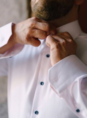 Damat, beyaz gömleğinin yakasını düğmeliyor. Yakın plan.
