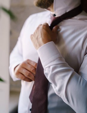 Damat beyaz bir gömleğin üzerine renkli bir kravat takar. Yakın plan.