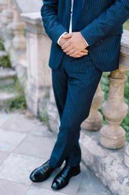 Takım elbiseli bir adam merdivenlerin yanında duruyor, korkuluklara yaslanıyor.