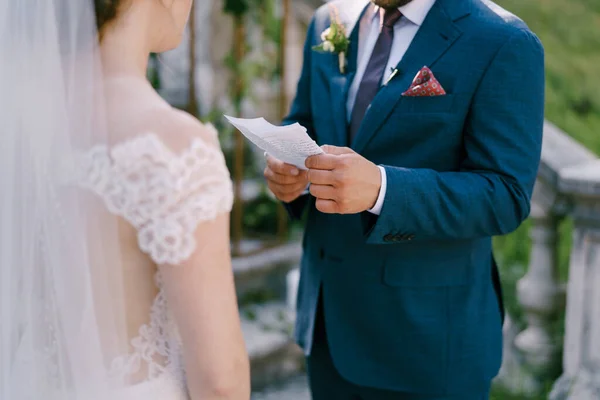 O noivo lê um juramento de uma folha de papel à noiva em um vestido branco. Close-up — Fotografia de Stock