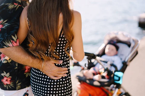 Pria memeluk wanita di depan kereta bayi dengan bayi. Tampilan belakang — Stok Foto