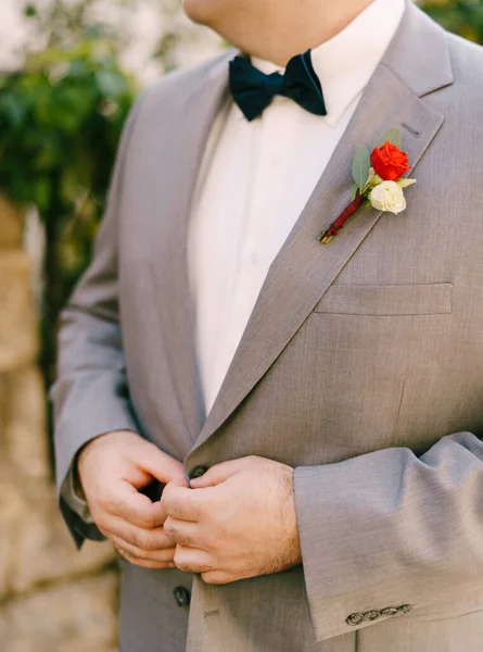 Bräutigam im grauen Anzug mit Boutonniere knöpft seine Jacke. Nahaufnahme — Stockfoto