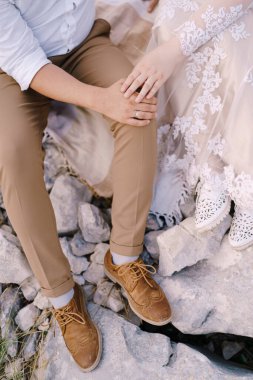 Gelin ve damat taşların üzerine oturup el ele tutuşurlar. Yakın plan.