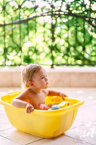 Il bambino si siede in una ciotola di acqua e giocattoli e alza lo sguardo — Foto Stock