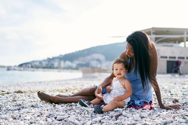 Ibu dengan seorang gadis kecil duduk di pantai dan memegang kerikil di tangan mereka — Stok Foto