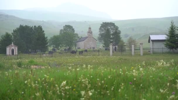 Kyrka och kyrkogård vid foten av bergen i en grön dal — Stockvideo