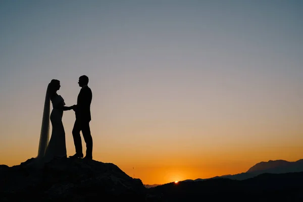Silhouettes of the bride and groom stand on the mountain against the background of the sunset — Stock Photo, Image