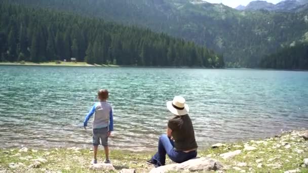 Mam en de jongen gooien kiezelstenen in het water van het Zwarte Meer. — Stockvideo