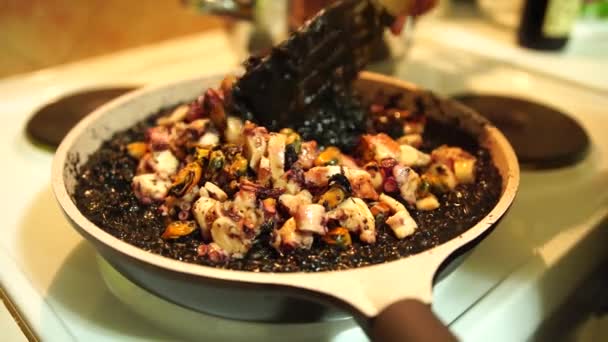 Stirring black risotto with sea food in pan on stove with spatula. Frying black risotto. — Stock Video
