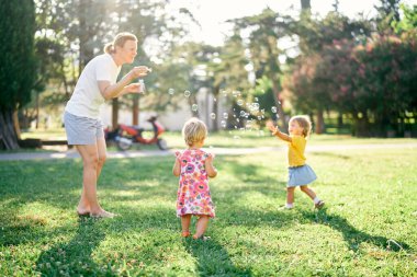 Kadın sabun köpüğü üflüyor ve iki küçük kız onları açıklıkta yakalıyor.