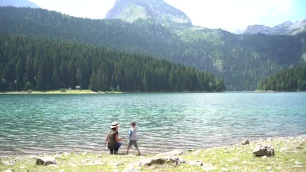 Мальчик бросает камешки рядом с матерью в воду Черного озера — стоковое видео
