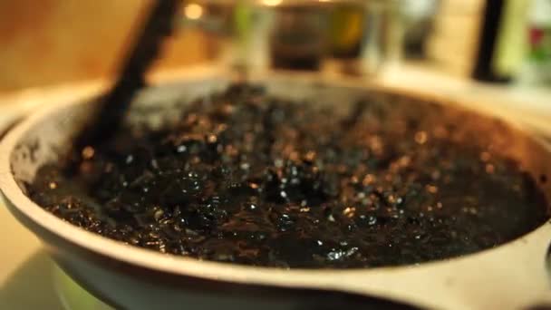 Míchání černého rizota v pánvi na sporáku s špachtlí. Vaření rýže pro černé rizoto. — Stock video