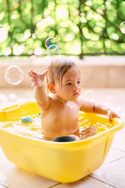 Il bambino cerca una bolla di sapone mentre è seduto in una ciotola d'acqua — Foto Stock