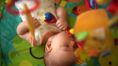 Yeni doğmuş bebek sırtında bir çıngırakla minderde oynuyor.