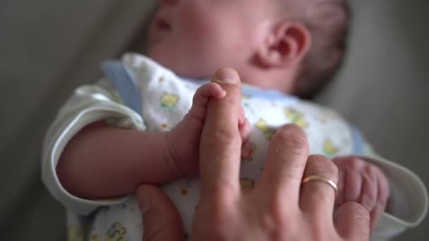 Ο νεογέννητος κρατάει τα χέρια του στα δάχτυλα της μαμάς ενώ είναι ξαπλωμένος στο κρεβάτι. — Αρχείο Βίντεο