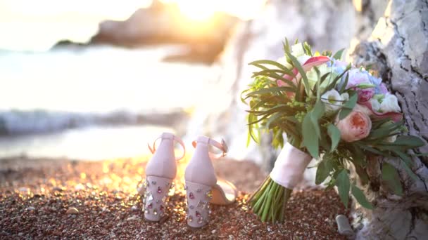 Bouquet da sposa e le scarpe da sposa si trovano vicino alla scogliera vicino al mare — Video Stock