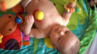 Yeni doğmuş bir bebek oyun hasırında yatar ve çıngırağı çiğner.