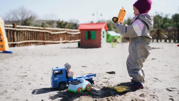 Küçük kız oyun parkında oyuncak bir arabadan kum döküyor. — Stok video