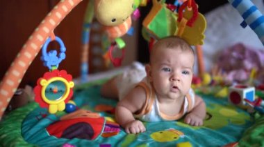 Yenidoğan karnının üstünde oyun hasırının üzerine yatar ve önüne bakar.