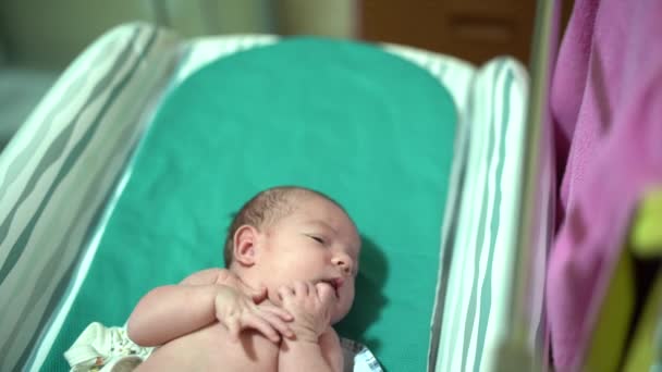 Bayi yang baru lahir terbaring di tempat tidur bayi dan menghisap jari kakinya — Stok Video