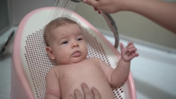 Novorozenec leží na skluzavce v koupelně a jeho matka mu myje hlavu ze sprchy — Stock video