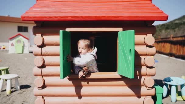 Niña en una casa de juguete abre y cierra ventanas — Vídeos de Stock
