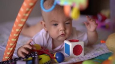 Bebek karnının üstünde oyun hasırına uzanıyor ve oyuncaklarla oynuyor.