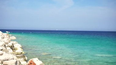 Martılar kayalık sahil kenarındaki açık mavi denizin üzerinde uçar.