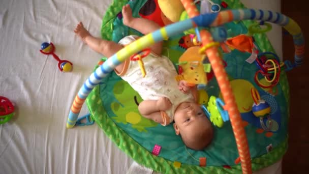 Yeni doğmuş bebek paspasın üzerine yatar ve oyuncakları çeker. Üst görünüm — Stok video
